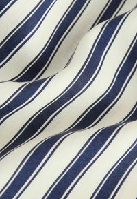 Tissu blanc avec des rayures verticales bleu marine espacées régulièrement, montrant des plis et des détails de texture.