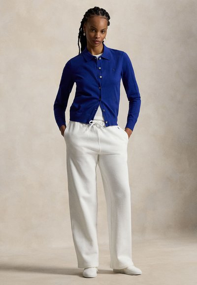 Μπλε καρώδ μπολερό με κουμπιά μπροστά, συνδυασμένο με παντελόνι εκρού με κορδόνι στη μέση. Με λεία υφή και στενή γραμμή, διαθέτει διακριτική λεπτομέρεια με λογότυπο.