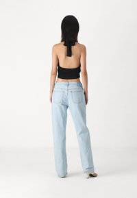 Black backless top with tie detail, paired with light blue wide-leg jeans. Material appears soft, with a relaxed fit and subtle stitching.