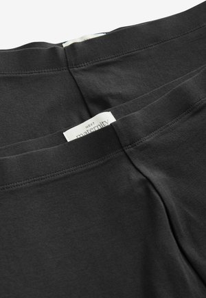 Juodos nėštumo legginsai, pagaminti iš minkšto, tampraus medvilnės. Su lygiu juosmeniu, ant kurio yra etiketė su užrašu "NEXT maternity."