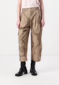 Beige patterned trousers with a pleated front, high waist, and wide legs, made from a textured fabric. Black ankle boots complement the look.