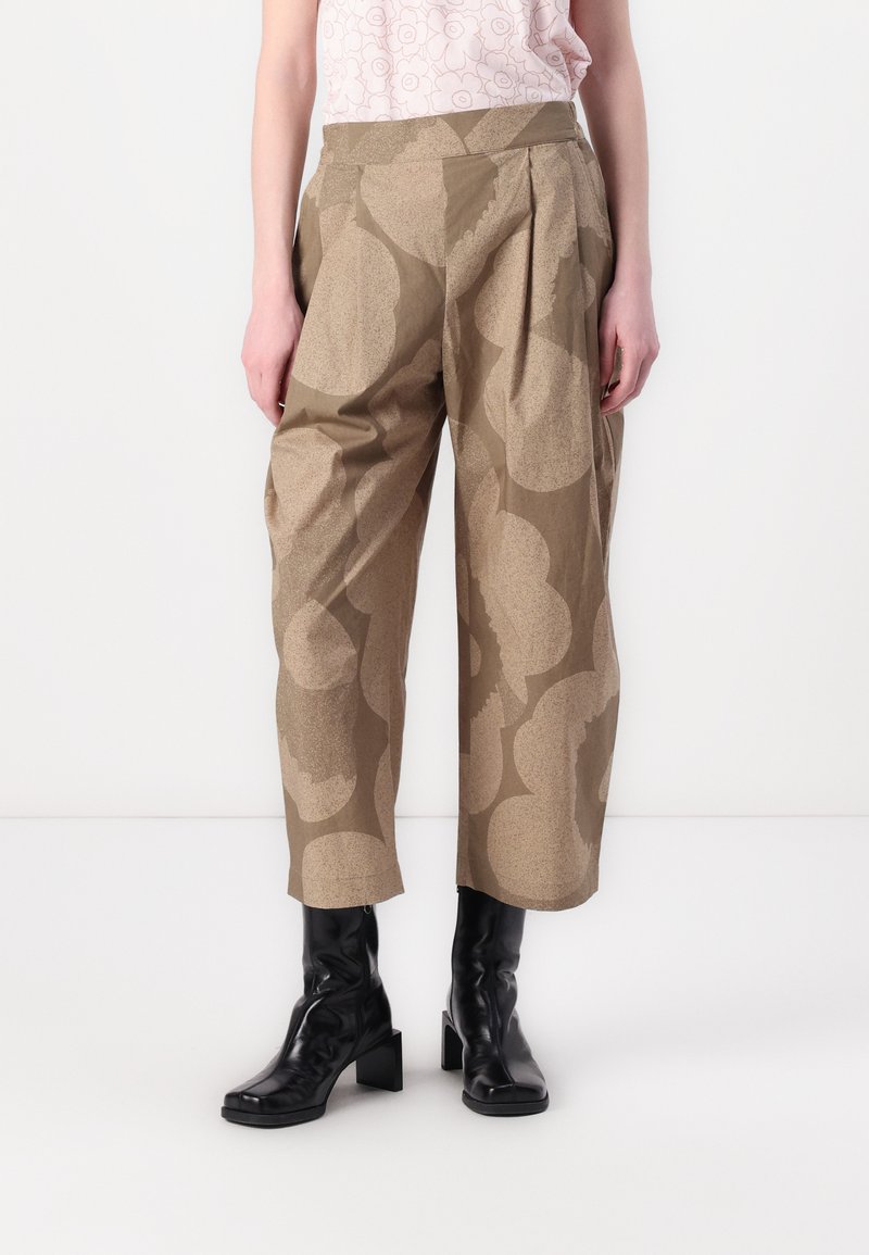 Beige patterned trousers with a pleated front, high waist, and wide legs, made from a textured fabric. Black ankle boots complement the look.