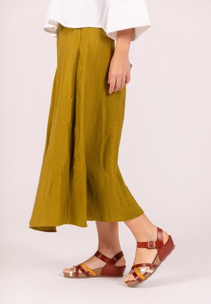 Olijfgroene, flowy midi-rok met een textuur. Gecombineerd met multikleurige strap-sandalen met een kurken sleehak.