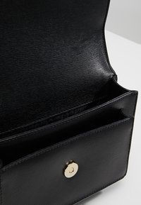 Černá kožená peněženka s texturovaným povrchem, otevřeným klopou a zlatým zapínáním na knoflík, ukazující více přihrádek uvnitř.