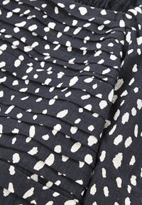 Crni materijal s bijelim točkicama ima vertikalne nabore, stvarajući teksturirani dizajn. Mekana pamučna tkanina s glatkom površinom.