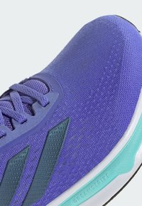 Zapatilla deportiva púrpura con parte superior de malla texturizada, acentos en azul claro y una suela blanca que presenta un detalle de amortiguación etiquetado como "DREAMSTRIKE".