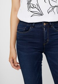 Mörkblå jeans i denim med slim fit, utrustade med dragkedja, knappstängning, fem fickor och subtila kontrastsömmar.