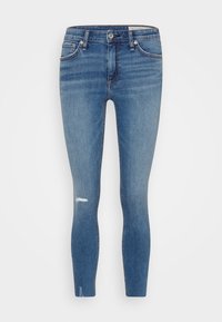 Vaqueros ajustados de mezclilla azul con una rodilla desgastada, diseño de cinco bolsillos y cremallera. La tela tiene una textura suave y un lavado medio.