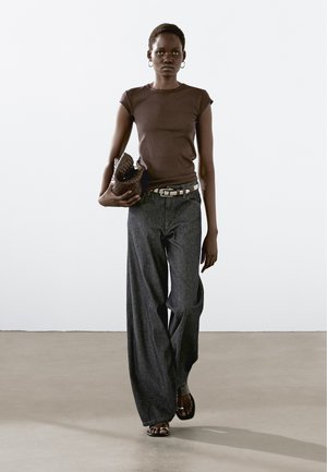 Brun, åtsittande t-shirt i kombination med vida, mörk denimjeans. Accessoarer med en texturerad brun clutch och ett silverfärgat nitarbälte.