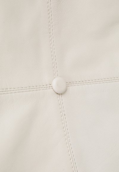 Bílé kožené čalounění s jemnou texturou, složitým prošíváním a centrálním knoflíkovým detailem, který zlepšuje celkový design.