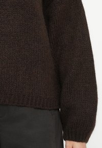 Hnědý pletený svetr s texturovaným, hrubým designem. Má dlouhé rukávy a ribbovaný lem. Materiál vypadá silný a útulný.