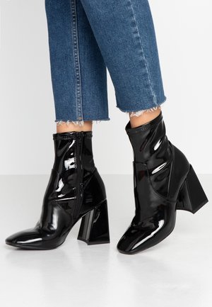 Bottines en cuir verni noir avec un bout pointu, dotées d'une fermeture éclair latérale et d'un talon bloc épais. Accents de design texturé.