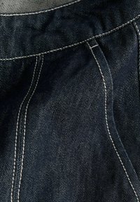 Mørkeblåt denimstof med hvide dobbelte sømme, der markerer en buet sømdetalje.