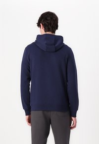 Sudadera azul marino con una textura suave, con un cuello trasero, mangas adaptadas y un dobladillo acanalado. Combinada con pantalones grises.