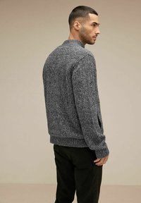 Gråstickad tröja med texturerad yta, rund halsringning och ribbade mudd och fåll. Kombineras med mörkfärgade byxor.