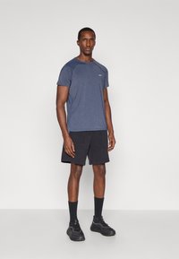 Conjunto de roupa desportiva: camisola de mangas curtas azul marinho, calções pretos com bolsos, meias pretas e sapatilhas desportivas. Design simples e funcional.