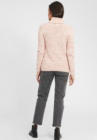 Light pink textured sweater with a cowl neck and ribbed cuffs, paired with gray trousers and black ankle boots, viewed from the back.