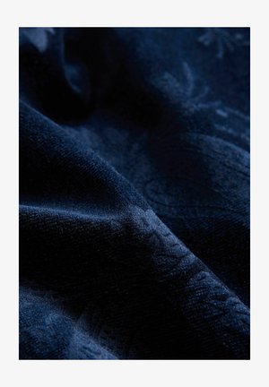 Dunkelblauer Textilstoff mit dezenten floralen Mustern und sanften Falten, die Tiefe und Schatten erzeugen.