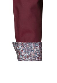 Manica di camicia bordeaux con polsini floreali che presentano motivi blu, rossi e bianchi. Il tessuto ha una consistenza liscia e una vestibilità strutturata.