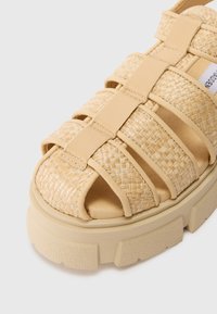 Beige kootud libistatavad sandaalid laiemate rihmadega, pehmendustega servadel ja paksu, tekstureeritud taldaga. Silmapaistev avatud varvaste disain.