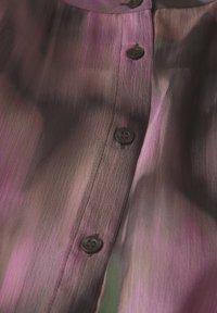 Durchsichtige Bluse in Lila- und Schwarz-Tönen, mit einer Knopfleiste mit dunklen Knöpfen und einem strukturierten, fließenden Stoffdesign.