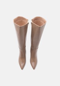 Botas de caña alta, con punta afilada, en suave cuero beige con un acabado brillante y doble cremallera lateral, que presentan un diseño estructurado y acentos de costura.