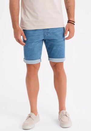Shorts en denim bleu clair avec des ourlets retroussés, présentant un design classique à cinq poches et une texture légèrement délavée. Portés avec des baskets claires.
