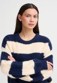 Maglione a righe blu navy e crema, realizzato in un morbido tessuto testurizzato. Presenta un collo rotondo a costine e maniche lunghe con ampie righe.