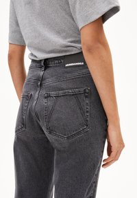 Zwarte denim jeans hebben een klassiek vijf-pocket ontwerp, textuurstof en een merklabel op de tailleband. De achterkant is weergegeven.