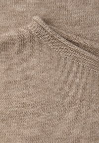 Beżowy dzianinowy tekstyl z miękką, fakturowaną powierzchnią, delikatnym wzorem oraz czystym, równym przeszyciem na krawędziach.