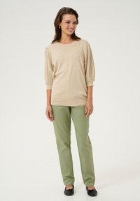 Beige knit top with ribbed balloon sleeves, paired with olive green straight-leg pants and black flats. Simple design, smooth texture.