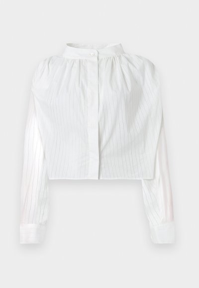 Λευκό μπλουζάκι cropped με μακριά μανίκια και λεπτές κάθετες ρίγες, με σούρες στο πάνω μέρος και ψηλό λαιμόκοψη με κλείσιμο με ένα κουμπί.