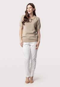 Beige gebreide poloshirt met korte mouwen, met een drie-knopen sluiting, gecombineerd met witte slim-fit broeken en beige sandalen met straps.