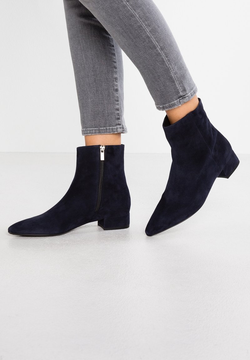 Personne portant un jean gris près du corps et des bottines en daim bleu marine foncé avec fermetures éclair latérales et talons blocs bas.