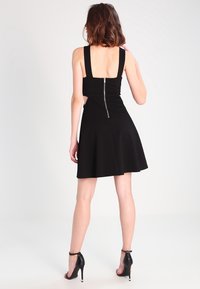 Svart ärmlös klänning med en figurnära bodice, utsvängd kjol och dragkedja i ryggen. Har utskärningar ovanför midjan och högklackade skor.