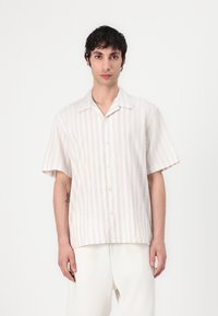 Κοντομάνικο, ανοιχτό μπεζ πουκάμισο με κάθετες λευκές ρίγες; διαθέτει ανοιχτό γιακά και χαλαρή εφαρμογή. Φτιαγμένο από ελαφρύ ύφασμα.