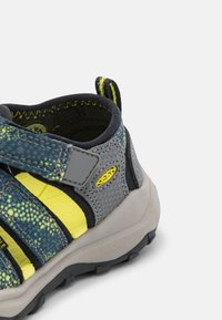 Scarpe da esterno per bambini in grigio e giallo neon. Presentano una tomaia in rete, una fascia in velcro, una suola in gomma testurizzata e un tallone rinforzato.