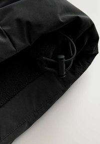 Schwarze, fleecegefütterte Tasche mit Kordelzug. Weicher Stoff, glatte Textur und saubere Nähte, die entlang der Kante sichtbar sind.