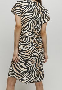 Kurzärmeliges Kleid mit einem schwarz-beigen Zebra-Print. Hergestellt aus weichem Stoff mit einer lässigen Passform und einer schmalen Taille für die Form.