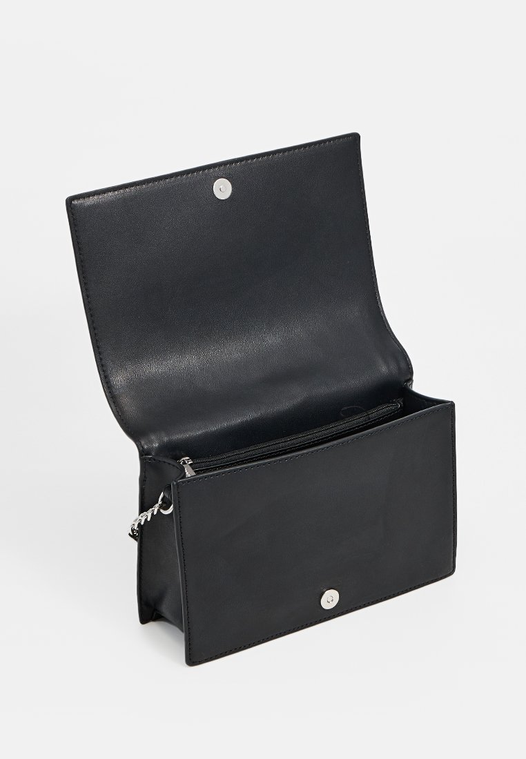 Sac en cuir noir avec un fermoir à pression, ouvert pour révéler un compartiment unique et une petite poche zippée à l'intérieur. Texture lisse, design minimal.