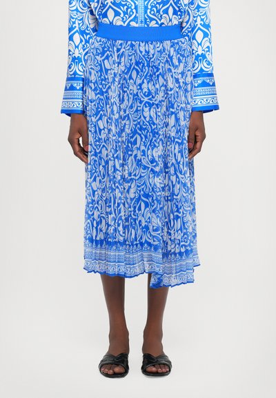 Jupe plissée bleue avec des motifs floraux blancs, une taille élastique et un ourlet avec des détails complexes. Associée à des sandales plates noires.