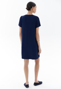 Marineblaues Kurzarmkleid mit rundem Halsausschnitt und lockerem Schnitt. Verfügt über eine glatte Textur und Detailnähte an der Rückseite, kombiniert mit marineblauen Schuhen.