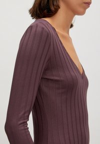 Langsleeves, diep V-hals top in diep paars, met verticale strepen voor textuur en een getailleerde silhouet.
