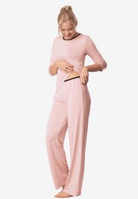 Jasnoróżowy zestaw piżamowy z długim rękawem, z czarnym wykończeniem oraz luźnymi spodniami o szerokich nogawkach z kieszeniami. Miękka faktura materiału.