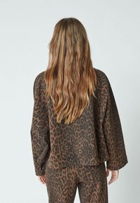 Brown leopard print jacket with a relaxed fit, long sleeves, and a curved hem. Made from soft fabric with a textured appearance.