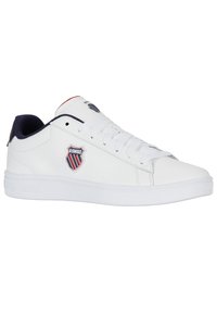 B baskets en cuir blanc avec un bout rond, une semelle en caoutchouc texturée blanche, des accents bleu marine et un patch logo arborant des bandes rouges, blanches et bleues.