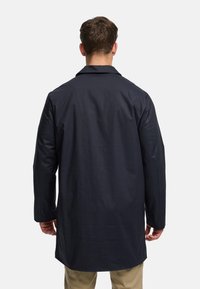 Mornarsko plavi kaput ravnog kroja, dugih rukava, s prorezom na leđima i glatke teksture. Minimalistički dizajn bez vidljivog hardvera ili ukrasa.