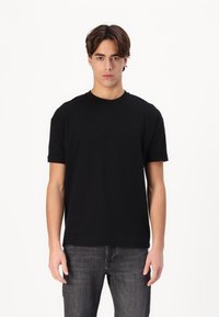 Svart kortermet t-skjorte laget av bomull, med rund hals, normal passform og oppbrettede ermer, sammen med mørke jeans.