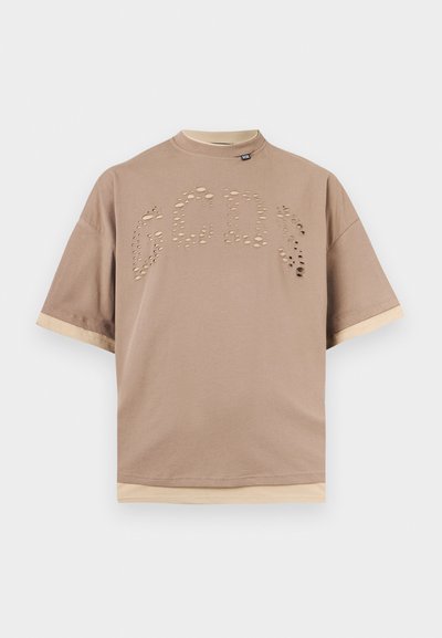 Μπεζ κοντομάνικο μπλουζάκι με στρωμένο τελείωμα και μανίκια, με τη λέξη «GCDS» σχηματισμένη από μικρές τρύπες στο στήθος.