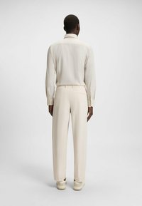 Camicia leggera crema con maniche lunghe e polsini con bottoni, abbinata a pantaloni con risvolto dello stesso colore. Tessuto morbido, vestibilità rilassata, design sobrio.